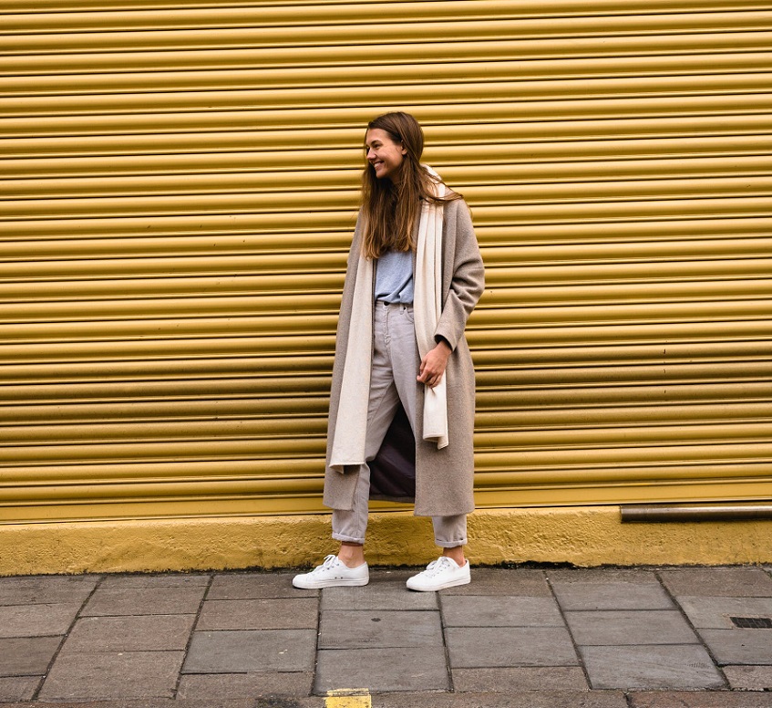 picture of a woman standing on a sidewalk wearing stylish clothes and sneakers in front a yellow background