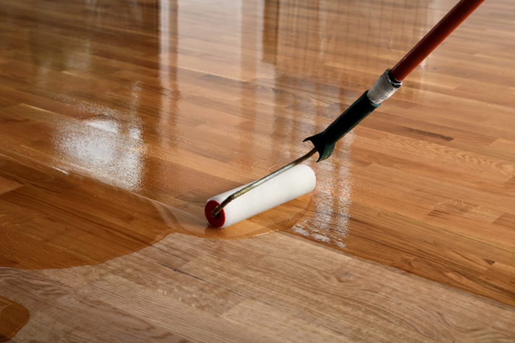 Lacquering wood floors. Worker uses a roller to coating floors. Varnishing lacquering parquet floor by paint roller - second layer. Home renovation parquet