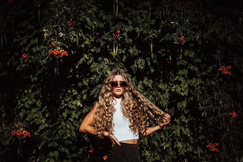 picture of a girl with a curly hair standing in front a greenery 