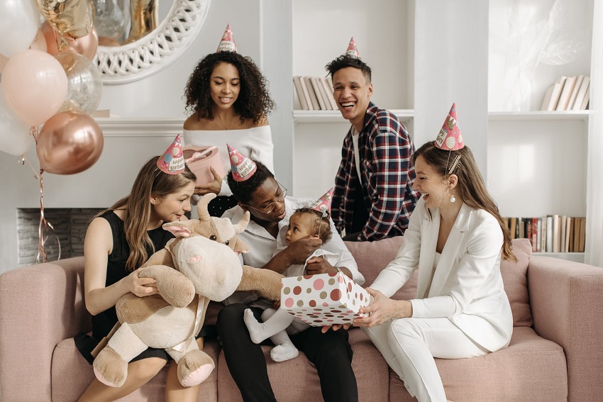 picture of people smiling, sitting on a sofa around a baby with gifts