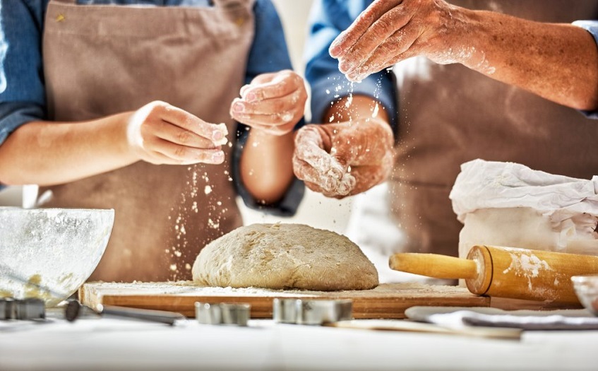 hands sprinkling wheat-free all purpose flour on dough 