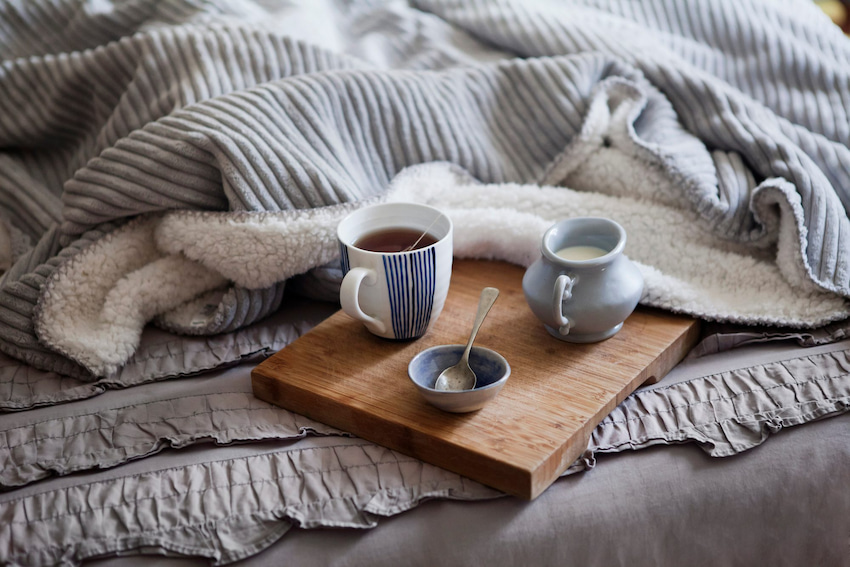 cup of decaf tea with milk and honey set on wooden board on bed