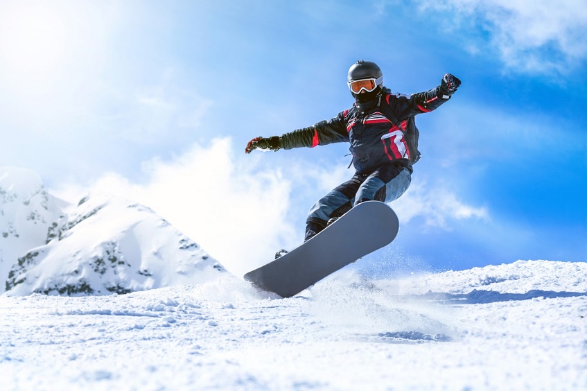 Man jumping with snowboard dressed in snowboard gear from mountain hill