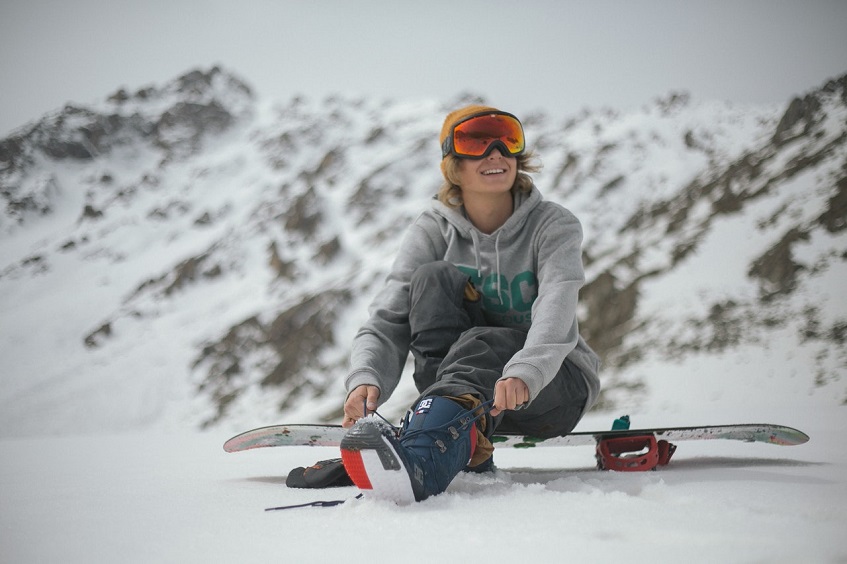 woman sitting on snowboard and tying her boot